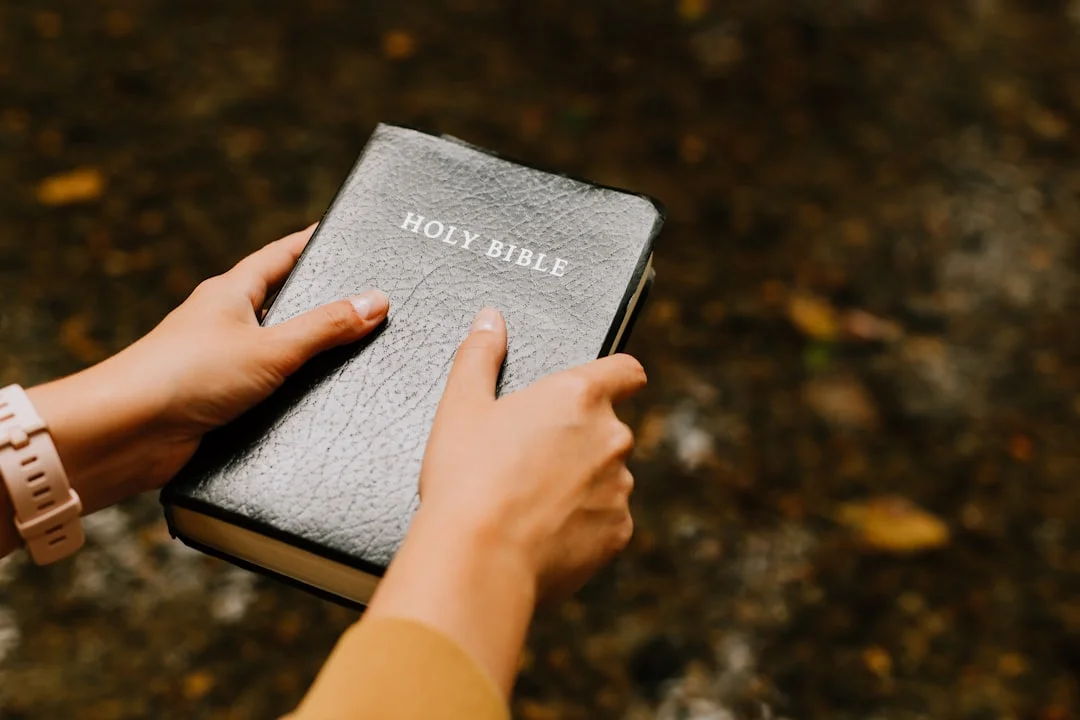 A warm flatlay of a personalized leather journal, a gold scripture pendant necklace, and a hand-lettered scripture print arranged on a linen surface with dried flowers and soft natural light